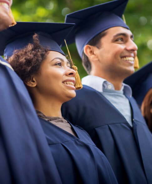 education, graduation and people concept - group of happy international students in mortar boards and bachelor gowns outdoors