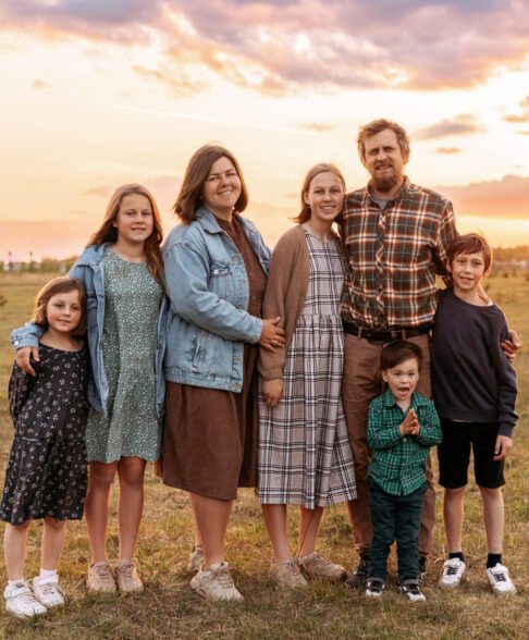 Large family of father, mother, two brothers and three sisters standing and sitting on a green field in summer, full length portrait.
