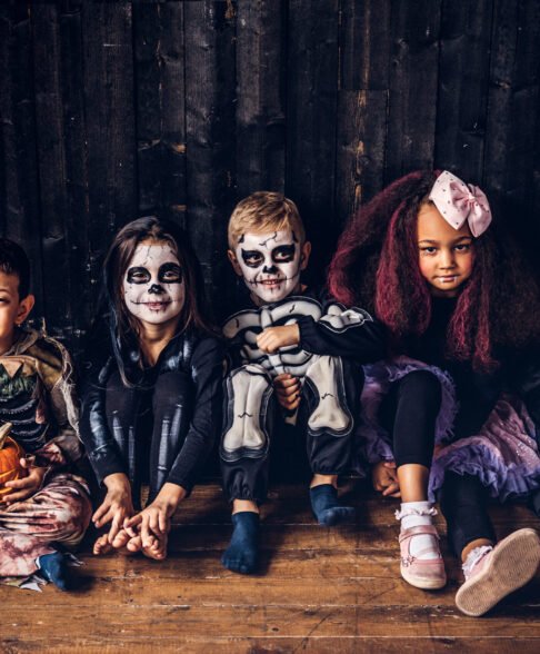 Halloween party with group children who sitting together on a wooden floor in an old house.