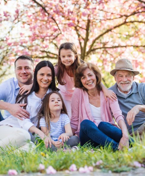 Front view of three generation family sitting outside in spring nature, looking at camera.